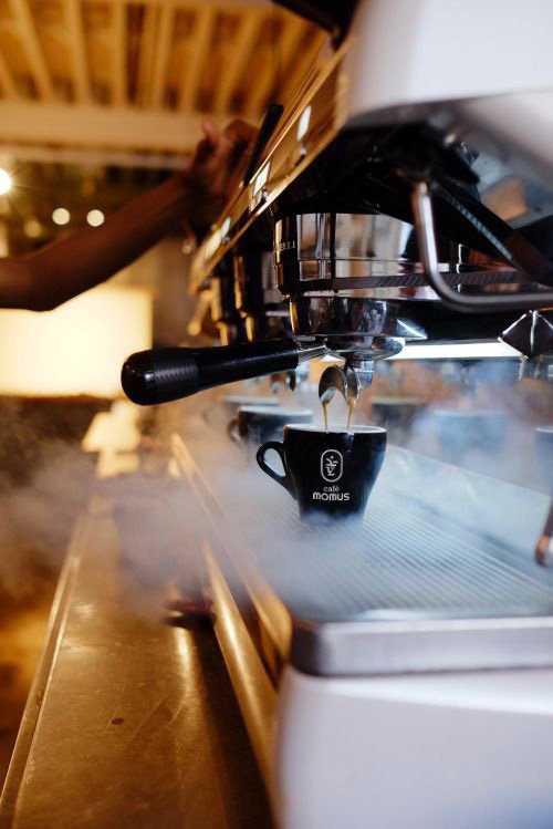 Espresso pouring into a black Café Momus cup, steam rising